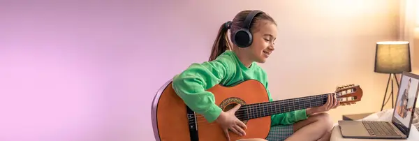 Little girl learns to play the guitar, music lesson with online teacher, distance learning to play the guitar. Web, social media banner template. Copy space.