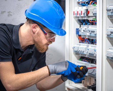 Elektrik santralinde fitilli çalışan erkek elektrik teknisyeni. Elektrik ekipmanlarının kurulumu ve bağlantısı.