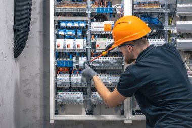Erkek bir elektrikçi elektrik kablosuyla santralde çalışıyor. Genç elektrikçi inşaat mühendisi sigorta kutusuna ekipman yerleştiriyor..