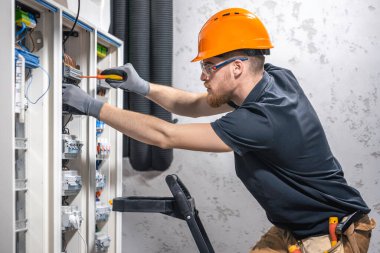 Bir erkek elektrikçi elektrik kablosuyla santralde çalışıyor..