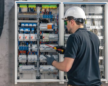 Erkek bir elektrikçi elektrik kablosu kullanarak bir santralde çalışır, ekipmanları aletlere bağlar. Arkadan bak..