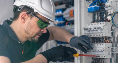 Erkek bir elektrikçi elektrik kablosu kullanarak bir santralde çalışır, ekipmanları aletlere bağlar..