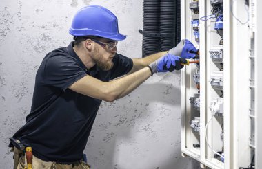 Elektrik santralinde fitilli çalışan erkek elektrik teknisyeni. Elektrik ekipmanlarının kurulumu ve bağlantısı.