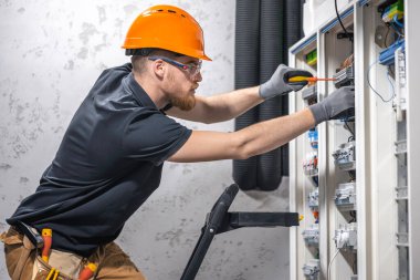 Bir erkek elektrikçi elektrik kablosuyla santralde çalışıyor..