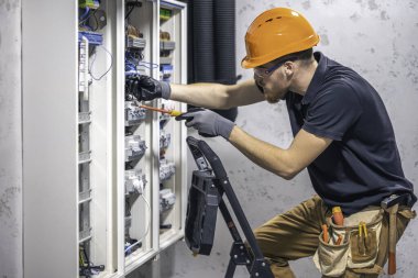 Erkek bir elektrikçi elektrik kablosuyla santralde çalışıyor. Tornavidalı elektrikçi sigorta kutusundaki elektrikli anahtar donanımını sıkılaştırıyor.