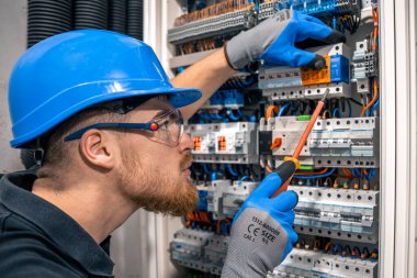 Male electrician working in a switchboard with fuses. Installation and connection of electrical equipment. Professional with tools in hand. clipart