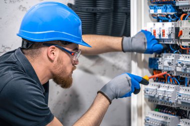 Elektrik santralinde fitilli çalışan erkek elektrik teknisyeni. Elektrik ekipmanlarının kurulumu ve bağlantısı.