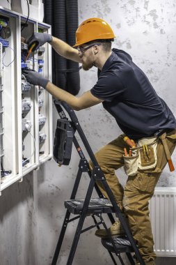 Erkek bir elektrikçi elektrik kablosuyla santralde çalışıyor. Tornavidalı elektrikçi sigorta kutusundaki elektrikli anahtar donanımını sıkılaştırıyor.
