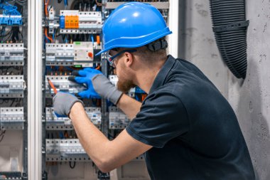 Erkek bir elektrikçi elektrik kablosuyla santralde çalışıyor. Tornavidalı elektrikçi sigorta kutusundaki elektrikli anahtar donanımını sıkılaştırıyor.