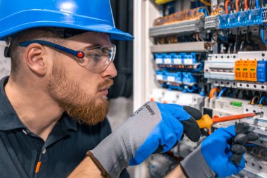 Elektrik santralinde fitilli çalışan erkek elektrikçi. Elektrik ekipmanlarının kurulumu ve bağlantısı. Elindeki aletlerle profesyonelce.