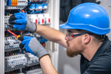 Erkek bir elektrikçi elektrik kablosuyla santralde çalışıyor. Tornavidalı elektrikçi sigorta kutusundaki elektrikli anahtar donanımını sıkılaştırıyor.