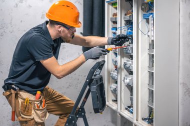 Erkek bir elektrikçi elektrik kablosuyla santralde çalışıyor. Tornavidalı elektrikçi sigorta kutusundaki elektrikli anahtar donanımını sıkılaştırıyor.