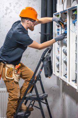 Erkek bir elektrikçi elektrik kablosuyla santralde çalışıyor. Tornavidalı elektrikçi sigorta kutusundaki elektrikli anahtar donanımını sıkılaştırıyor.