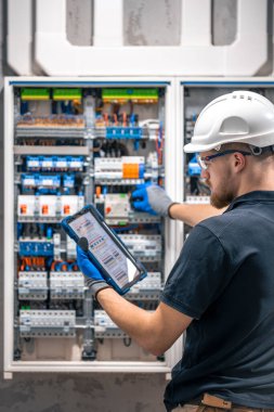 Elektrik teknisyeni sigortalı bir santralde çalışıyor, tablet kullanıyor. Elektrik teknisyeni sigortalı bir santralde çalışırken odaklanmış görünüyor.