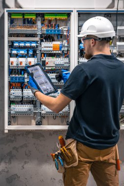 Elektrik teknisyeni sigortalı bir santralde çalışıyor, tablet kullanıyor. Elektrik teknisyeni sigortalı bir santralde çalışırken odaklanmış görünüyor.