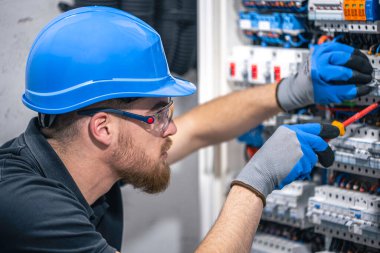 Erkek bir elektrikçi elektrik kablosuyla santralde çalışıyor. Tornavidalı elektrikçi sigorta kutusundaki elektrikli anahtar donanımını sıkılaştırıyor.