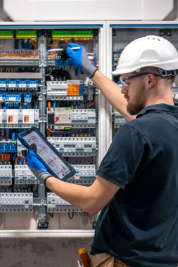 Elektrik teknisyeni sigortalı bir santralde çalışıyor, tablet kullanıyor. Elektrik teknisyeni sigortalı bir santralde çalışırken odaklanmış görünüyor.
