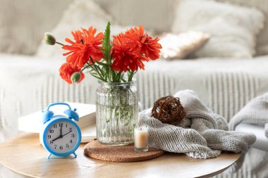 İçinde bir buket haşhaş, çalar saat ve kitap bulunan ev kompozisyonu.