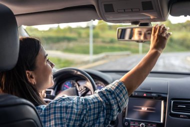 Çekici genç bir kadın araba kullanıyor, içeriden bakıyor. Bir kadın sürücü arabadaki aynaya dokunuyor. Uzun yol kavramı, arabayla seyahat etmek..