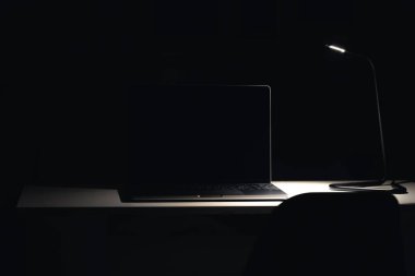 Gece karanlık bir odada siyah dizüstü bilgisayar ekranı. Geceleri masadaki bilgisayar dizüstü bilgisayarı ile çalışma alanı, boşluğu kopyala.