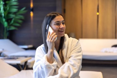Genç bir kadın spa kompleksinde rahatlıyor ve akıllı telefon kullanıyor. Masaj terapisti hizmeti kavramı.