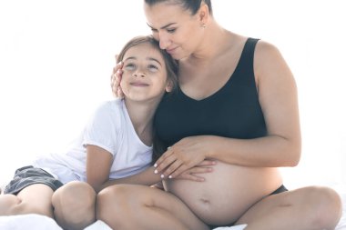 Hamile bir kadın ve genç kızı yatakta oturuyorlar. Hamile anne ve kızı evde dinleniyor. Annelik ve ebeveynlik kavramı.