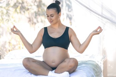 Nilüfer çiçekli hamile bir kadın sağlıklı hamilelik için meditasyon ya da nefes alma egzersizleri yapıyor ve vücudu doğuma hazırlıyor. Genç hamile anne evde yoga yapıyor..