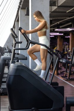 Beyaz spor giysili güçlü kadın ısınma antrenmanı için spor salonundaki koşu bandı tırmanma makinesinde koşuyor..