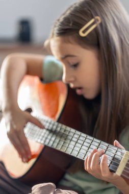 Kız gitar çalıyor. Gitarlı küçük bir kız. Yüksek kalite fotoğraf. Evde gitar çalıyorum. Küçük bir kız şarkı söyler ve gitar çalar..