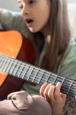 Kız gitar çalıyor. Gitarlı küçük bir kız. Yüksek kalite fotoğraf. Evde gitar çalıyorum. Küçük bir kız şarkı söyler ve gitar çalar..