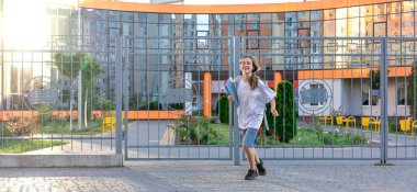 Gözlüklü güzel liseli kız sırtında sırt çantasıyla okuldan kaçıyor. Okul günbatımının arka planında. Okul malzemeleriyle. Yüksek kalite fotoğraf