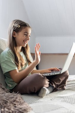 Bir liseli kız evde çevrimiçi çalışıyor. İnternetten okul eğitimi. Yüksek kalite fotoğraf. Kız öğretmene internetten ödevinden bahsediyor..