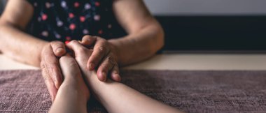 Tanınmayan bir kadın yaşlı bir bayana ilgi gösteriyor. Aile değerleri kavramı. Yüksek kalite fotoğraf. Kızı ve yaşlı annesinin elleri. Yakın plan. Metin için boşluk.