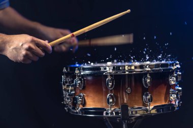 Davul sopaları trampet davuluna siyah arka planda su sıçratarak çarpıyor. Yüksek kalite fotoğraf. Erkeklerin elleri davulda çubuk çalar. Bir adam davul çalıyor..