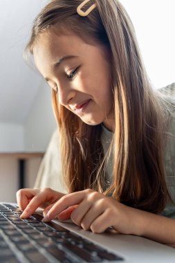 Bir liseli kız evde çevrimiçi çalışıyor. İnternetten okul eğitimi. Yüksek kalite fotoğraf. Kız dizüstü bilgisayarın klavyesinde yazıyor..