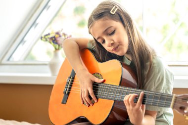 Kız gitar çalıyor. Gitarlı küçük bir kız. Yüksek kalite fotoğraf. Evde gitar çalıyorum. Küçük bir kız şarkı söyler ve gitar çalar..