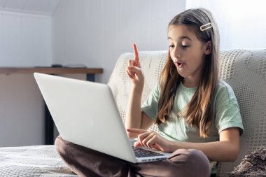 Bir liseli kız evde çevrimiçi çalışıyor. İnternetten okul eğitimi. Yüksek kalite fotoğraf. Kız öğretmene internetten ödevinden bahsediyor..