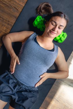 Hamile bir kadın, spor salonunda, bir paspasın üzerinde, masaj rulosuyla. Rahatlama ve masaj rulosuyla ısınma. Yüksek kalite fotoğraf. Üst görünüm