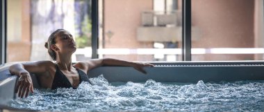 Genç bir kadın jakuzide dinleniyor. Mesaj için yer var. Yüksek kalite fotoğraf. Jakuzide rahatlama. Havuzda yüzen bikinili pozitif kadın..