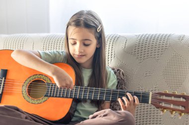 Kız gitar çalıyor. Gitarlı küçük bir kız. Yüksek kalite fotoğraf. Evde gitar çalıyorum. Küçük bir kız şarkı söyler ve gitar çalar..