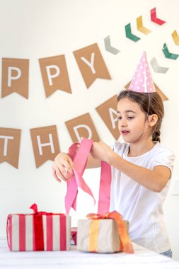 Tatlı bir kız tatil hediyelerini açar. Doğum günü konsepti. Yüksek kalite fotoğraf. Renkli hediyeler. Evde doğum günü partisi. Tatil şapkalı bir kız..