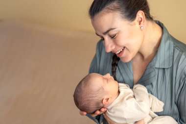 Yeni doğmuş bir bebeği olan genç bir anne. Yeni doğmuş bebek. Yüksek kalite fotoğraf. Annelik. Anne ve bebek evde. Bir anne yeni doğmuş bir bebeği kollarında tutar. Metin için boşluk.