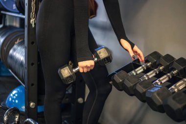 Spor salonundaki genç kadın. Spor salonunda dambıllar. Spor salonu. Yüksek kalite fotoğraf. Salondaki dambılı kız. Dambıllı eller yakın plan.