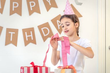 Tatlı bir kız tatil hediyelerini açar. Doğum günü konsepti. Yüksek kalite fotoğraf. Renkli hediyeler. Evde doğum günü partisi. Tatil şapkalı bir kız..