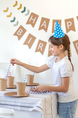 Kız doğum günü için festival masasını süslüyor. Doğum günü konsepti. Yüksek kalite fotoğraf. Şenlik şapkalı bir kız. Arka planda mutlu yıllar..