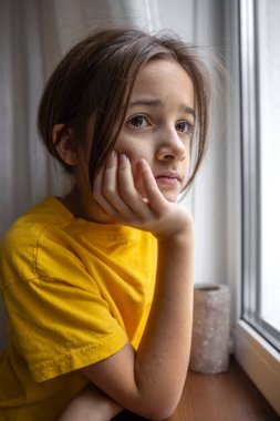 Kasvetli ve üzgün bir kız pencereden dışarı bakar. Duygular konsepti. Yüksek kalite fotoğraf. Duygusal hüzünlü yakın çekim. Kızın hüzünlü düşünceleri var..