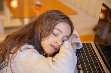 Masada uyuyan çok çalışan ve yorgun bir kız. Dizüstü bilgisayarı olan bir kız. Yüksek kalite fotoğraf. Dizüstü bilgisayardaki yorgun kız. Dizüstü bilgisayarda aşırı yüklenme.