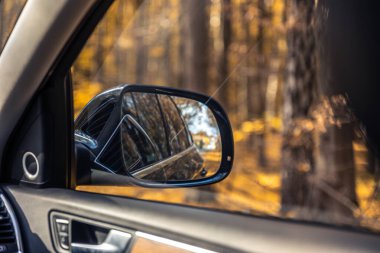 Bir arabanın dikiz aynası. Dikiz aynasından görüldü. Yüksek kalite fotoğraf. Seyahat konsepti. Araba ve ayna. Yolculuk. Sonbahar mevsimidir. Sonbahar yaprakları.