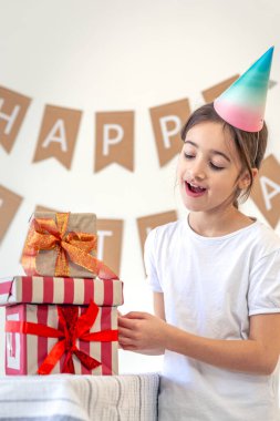 Tatlı bir kız tatil hediyelerini açar. Doğum günü konsepti. Yüksek kalite fotoğraf. Renkli hediyeler. Evde doğum günü partisi. Tatil şapkalı bir kız..