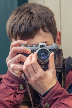Genç bir adam eski bir kamerayla fotoğraf çekiyor. Film kamerası fotoğrafçılığı. Yüksek kalite fotoğraf. Adamın biri sokaktaki klasik bir film kamerasıyla fotoğraf çekiyor. Bir adam elinde antika bir kamera tutuyor..